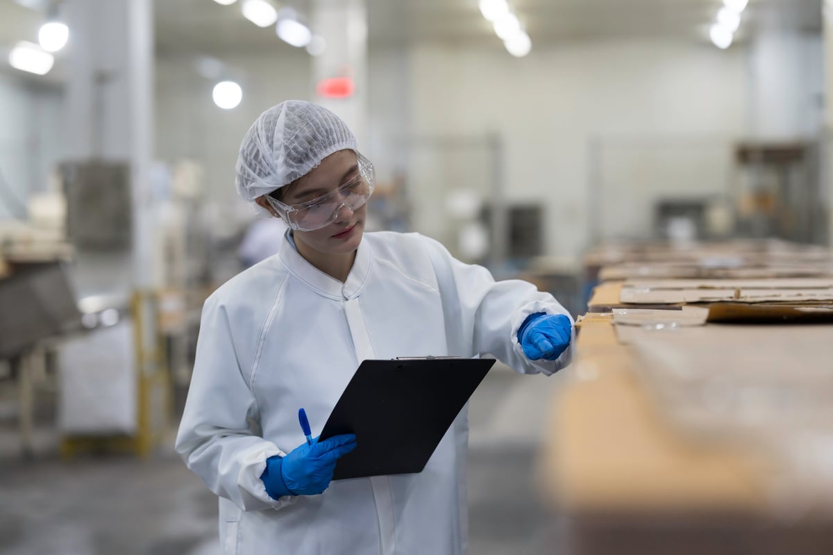 Inspector in protective clothing examining packaging components against a checklist on a production line