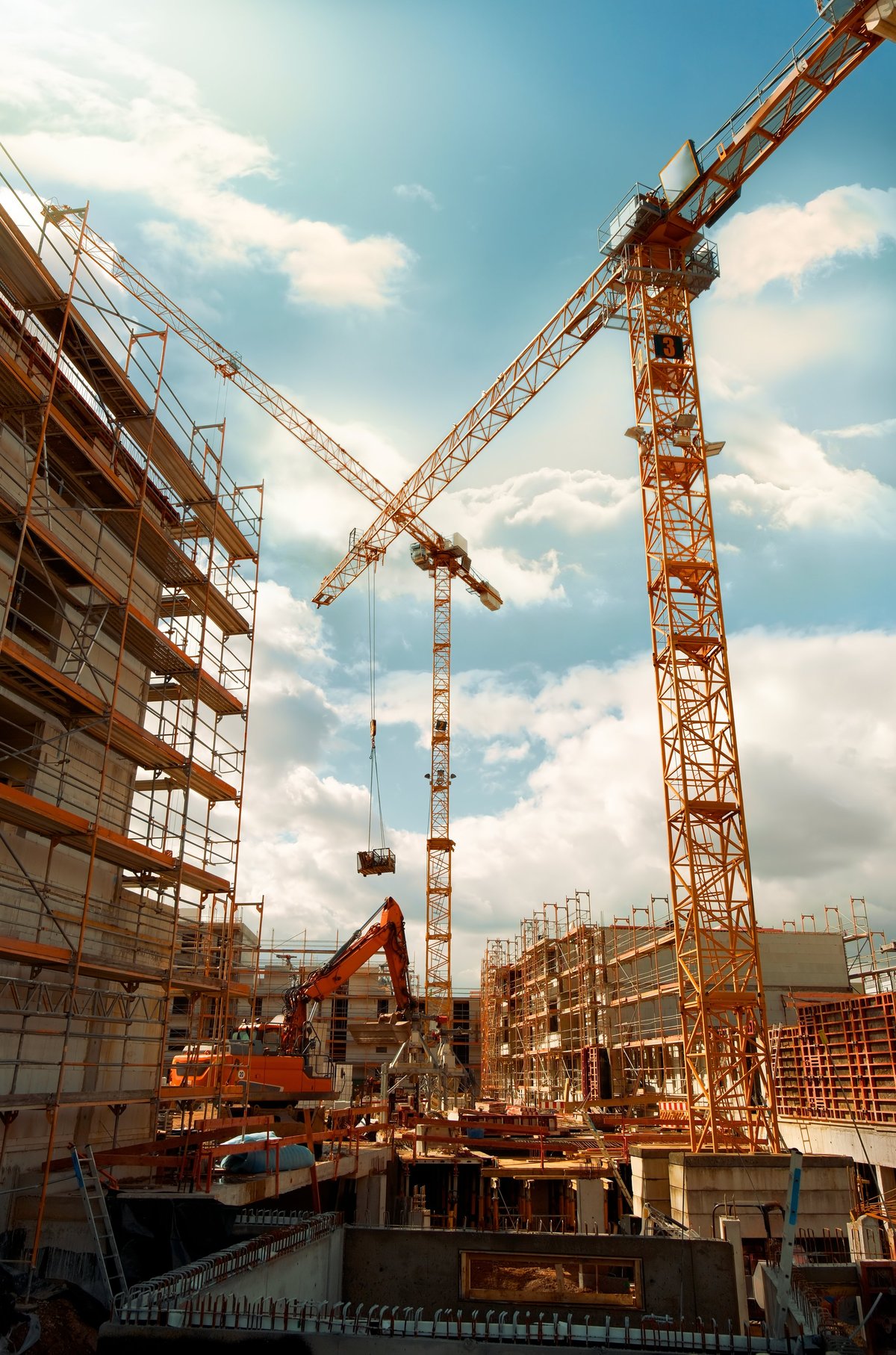 A construction site with cranes against a blue sky, viewed from a wide upward angle