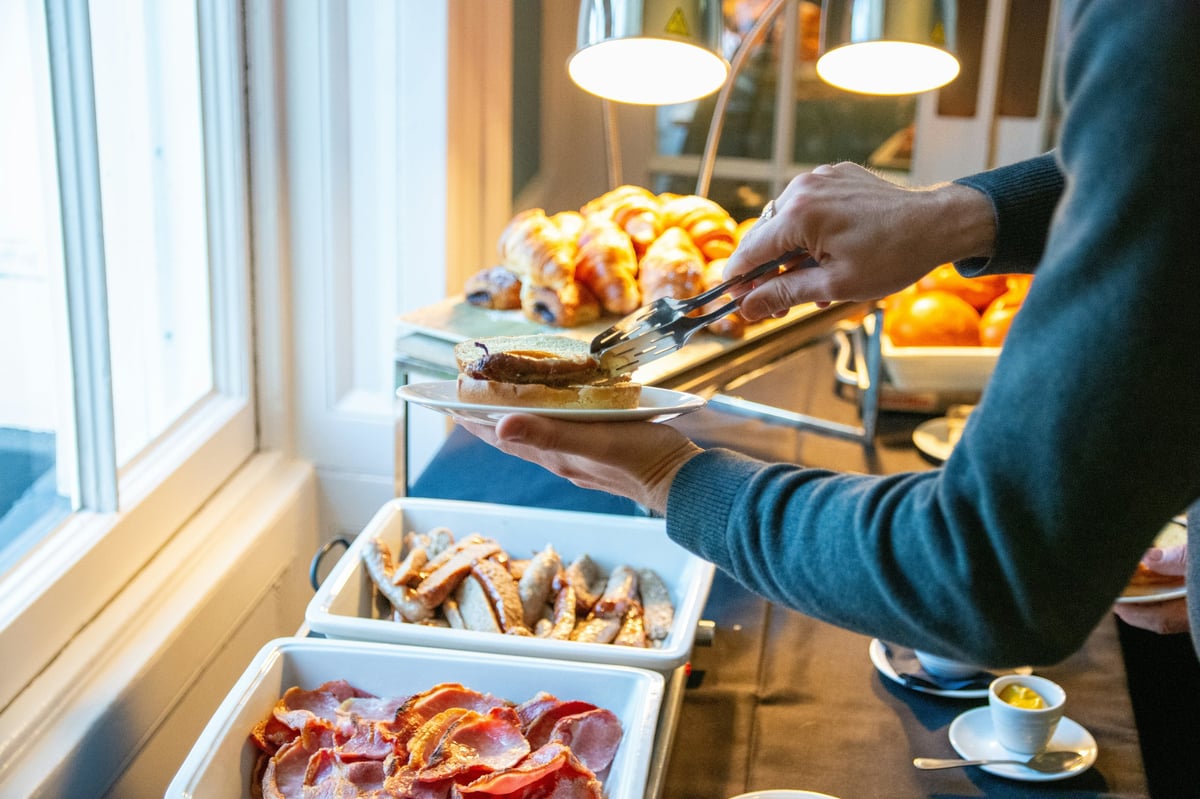 A guest using serving tongs to select breakfast at a buffet