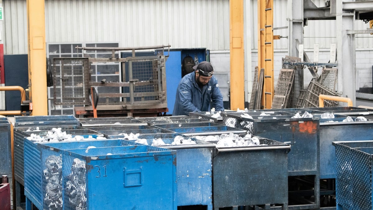 Worker handling metal components in large bins inside a factory