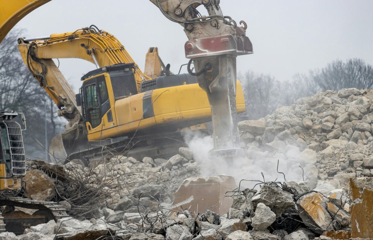 Excavators and a hydraulic breaker working among concrete rubble and exposed reinforcing steel