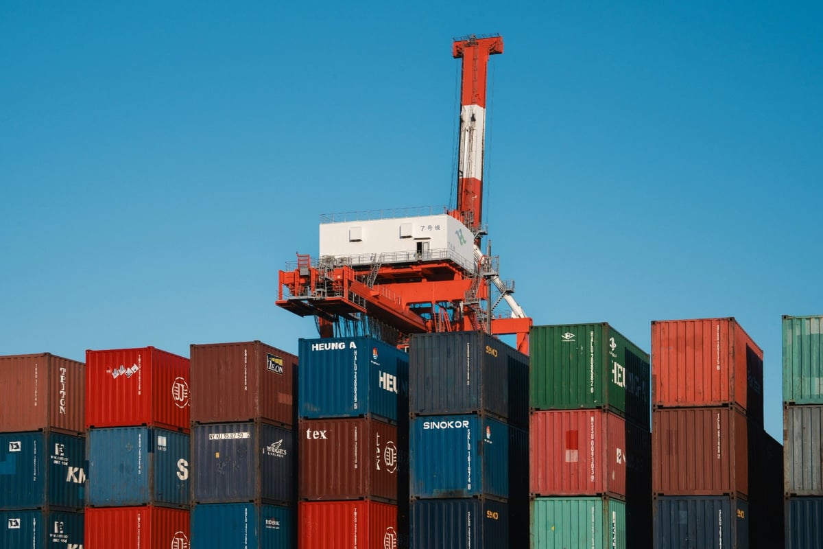 Stacked freight containers beneath a red and white port crane