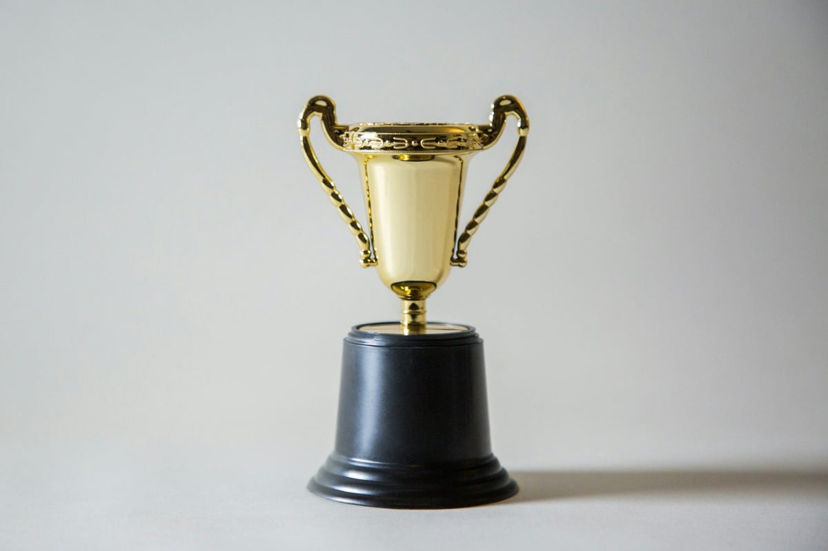 Gold trophy with curved handles and a black base against a pale background