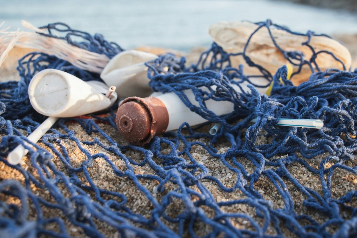 Discarded plastic cups and straws tangled with blue netting on sand